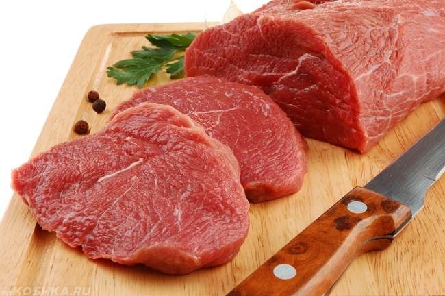 Кусок красного разрезанного ножом мяса на доске